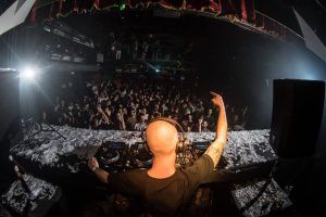 En el City Hall de Barcelona, un DJ con auriculares dinamiza a la animada multitud bajo luces vibrantes y confeti en espiral, creando una noche inolvidable. - ForTwo - Planes para parejas