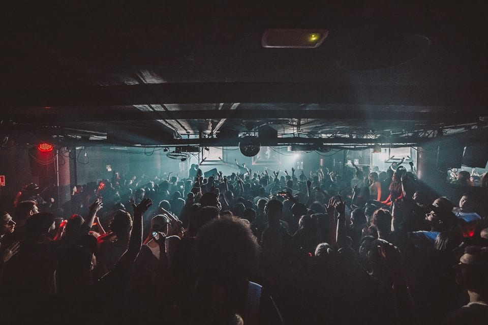 En City Hall Barcelona, una vibrante discoteca, la gente baila con las manos en alto bajo luces tenues, haciendo eco de la enérgica vida nocturna. - ForTwo - Planes para parejas