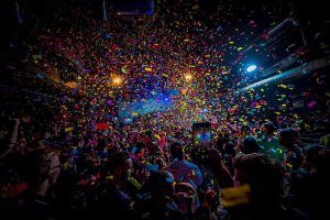 Una multitud animada baila en un concierto cerca del Ayuntamiento de Barcelona, rodeada de confeti de colores en un lugar poco iluminado. - ForTwo - Planes para parejas