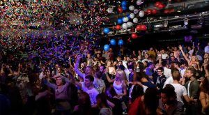 El ambiente animado de una celebración en el Ayuntamiento de Barcelona se captura con confeti y globos de colores mientras la gente baila y disfruta de cada momento vibrante juntos. - ForTwo - Planes para parejas