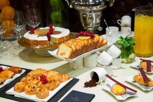 Una variedad de pasteles, tartas y croissants enriquece la mesa del Hotel Casa Fuster GL Monumento (Barcelona), acompañados de tazas, zumo de naranja y una cafetera de plata: un auténtico testimonio del sabor. - ForTwo - Planes para parejas