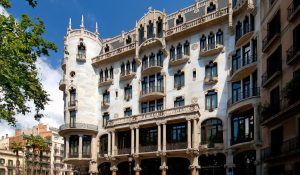 El edificio ornamentado, que refleja el encanto de Barcelona, presenta torres redondeadas, balcones y fachadas decorativas bajo un cielo azul claro, similar al Hotel Casa Fuster GL Monumento (Barcelona). - ForTwo - Planes para parejas