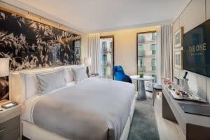 Disfrute de la comodidad del Hotel The One Barcelona GL en una elegante habitación con una cama grande, cautivadora decoración mural, televisor y silla. Relájese en la pequeña mesa redonda junto a la ventana con vistas a la ciudad para disfrutar de un ambiente sereno y unas vistas impresionantes. - ForTwo - Planes para parejas