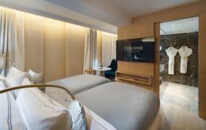 El One Barcelona GL ofrece una moderna habitación con dos cómodas camas, un televisor grande y una acogedora zona de estar. Una puerta abierta conduce al baño, equipado con suaves albornoces. - ForTwo - Planes para parejas