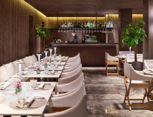 El elegante restaurante del Hotel The One Barcelona GL cuenta con filas de sillas blancas, mesas preparadas y un barman en un bar bien surtido, lo que muestra el encanto sofisticado del hotel. - ForTwo - Planes para parejas