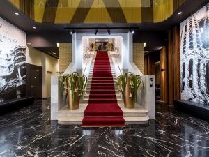 El Hotel Vincci Gala de Barcelona cuenta con una gran escalera con alfombra roja, barandillas ornamentadas y plantas en macetas que realzan su ambiente lujoso. - ForTwo - Planes para parejas