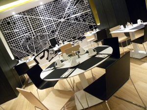 La elegante cafetería del Hotel Vincci Gala cuenta con una elegante decoración en blanco y negro, diseños geométricos en las paredes y mesas y sillas perfectamente dispuestas. Ideal para disfrutar de la elegancia moderna de Barcelona. - ForTwo - Planes para parejas