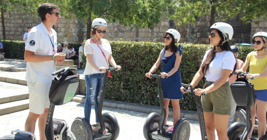 Cinco personas con cascos en Segways junto a un guía disfrutan de un día soleado en Sevilla. La Ruta en Segway por Sevilla ofrece una forma aventurera de explorar las vibrantes calles de la ciudad. - ForTwo - Planes para parejas