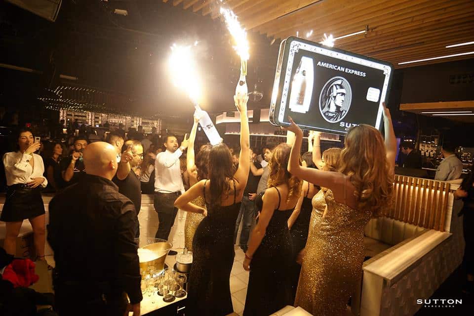 En el vibrante club Sutton de Barcelona, los asistentes celebran con bengalas, un gran juego de cartas y mujeres elegantemente vestidas, lo que realza el ambiente festivo. - ForTwo - Planes para parejas