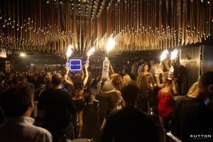 El club Sutton de Barcelona vibra con energía mientras una vibrante pista de baile cobra vida con la música, las bengalas brillan en manos entusiastas y un techo moderno y elegante proyecta un brillo encantador sobre la escena. - ForTwo - Planes para parejas