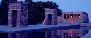 Un majestuoso templo de piedra con un estanque reflectante al anochecer, ubicado entre árboles y suavemente iluminado bajo el cielo crepuscular, proporciona un telón de fondo encantador para el "Tour panorámico por Madrid en autobús de lujo", que muestra los cautivadores paisajes de Madrid. - ForTwo - Planes para parejas