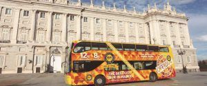 El Tour panorámico por Madrid en autobús de lujo presenta un autobús de dos pisos estacionado frente a un gran edificio histórico blanco bañado por la luz del día. - ForTwo - Planes para parejas