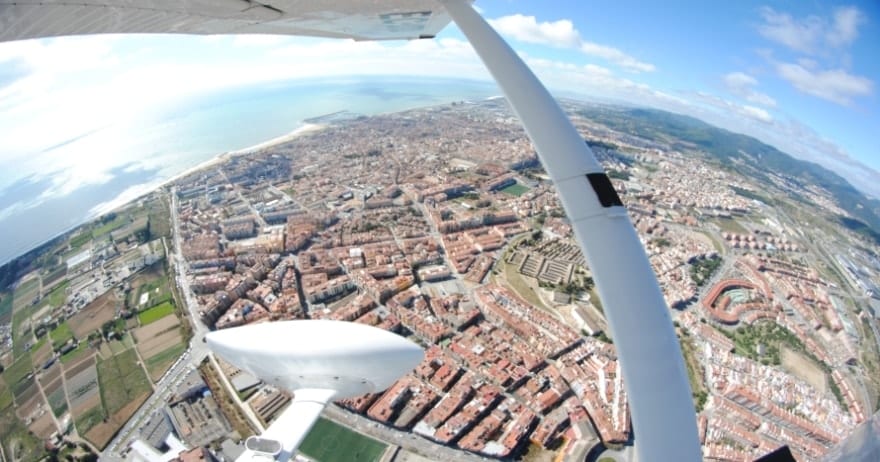 Experimente una vista aérea en un "Vuelo de iniciación en avióneta por Montserrat (Barcelona)" destacando los edificios, las carreteras y el océano de una ciudad costera. - ForTwo - Planes para parejas