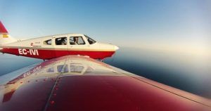 Una avióneta roja y blanca vuela sobre el océano cerca de Montserrat (Barcelona), vista desde el ala de otro avión bajo un cielo azul claro, recordando una serena experiencia del "Vuelo de iniciación en avióneta por Montserrat (Barcelona). - ForTwo - Planes para parejas