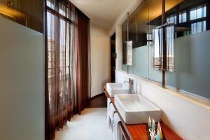 El Wilson Boutique Hotel de Barcelona cuenta con un moderno baño con dos lavabos, un gran espejo, paneles de vidrio esmerilado y elegantes cortinas marrones junto a la ventana. - ForTwo - Planes para parejas