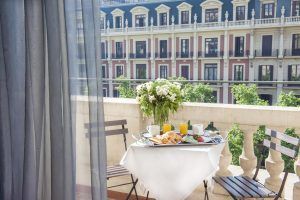 Disfrute de un desayuno con croissants y bebidas en el balcón del Wilson Boutique Hotel (Barcelona), admirando la elegante arquitectura de la ciudad y su exuberante vegetación bajo un cielo soleado. - ForTwo - Planes para parejas