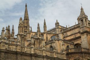 La majestuosa Catedral de Sevilla, de estilo gótico, adornada con agujas y arcos de piedra ornamentados bajo un cielo nublado, ofrece la experiencia de "Visita la Catedral de Sevilla sin esperas" para aquellos deseosos de apreciar su esplendor histórico. - ForTwo - Planes para parejas