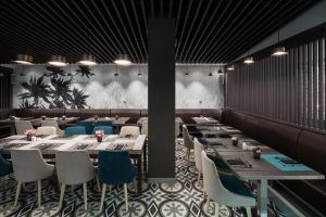 Ubicado en el centro de Barcelona, el Hotel Catalonia Magdalenes cuenta con un moderno restaurante con suelo estampado, sillas grises y azules, un techo oscuro y una iluminación suave sobre cada mesa, ofreciendo una experiencia gastronómica ideal. - ForTwo - Planes para parejas