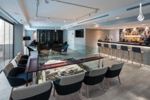 Explora el salón contemporáneo del Hotel Catalonia Magdalenes en Barcelona, que cuenta con un elegante bar, una mesa de acuario, cómodas sillas y un televisor rodeado de un elegante diseño minimalista. - ForTwo - Planes para parejas