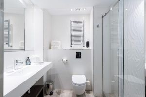 El Hotel Catalonia Magdalenes de Barcelona cuenta con un elegante baño con un moderno diseño blanco, ducha de cristal, inodoro montado en la pared y lavabo con un gran espejo. - ForTwo - Planes para parejas