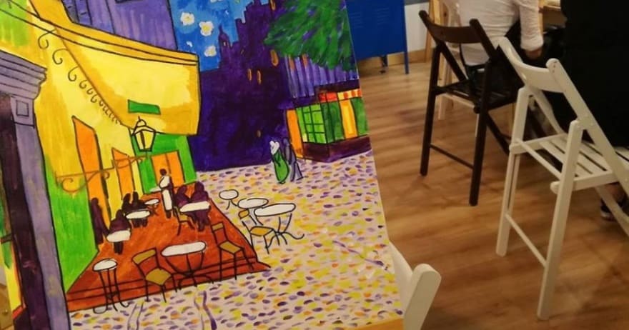 Una pintura colorida sobre un caballete captura una escena de café con sillas plegables, evocando la esencia vibrante de Madrid, que recuerda a un Taller creativo de pintura de cuadros. - ForTwo - Planes para parejas