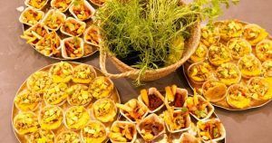 Bandejas de pastelitos variados y aperitivos, elaborados por Taller 24 en su Taller de cocina en Sants (Barcelona), rodean una cesta de verduras en el centro. - ForTwo - Planes para parejas
