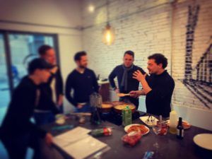 Cinco personas se reunieron alrededor de la barra de la cocina de un acogedor apartamento en Sants, Barcelona, para disfrutar de una animada conversación durante un taller práctico de cocina en Sants con Taller 24. La mesa, decorada con exquisita comida y bebidas, realzaba el cálido ambiente. - ForTwo - Planes para parejas