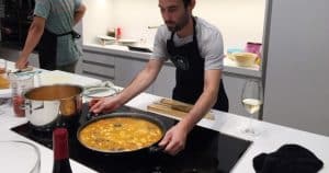 En una acogedora cocina inspirada en la vibrante escena gastronómica de Barcelona, alguien remueve una gran sartén con sabrosos ingredientes. Cerca, el vino y las ollas están cuidadosamente dispuestos, evocando las delicias culinarias del Taller de Cocina en la Illa Diagonal. - ForTwo - Planes para parejas