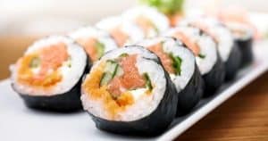 Primer plano de rollos de sushi con salmón, pepino y arroz en un plato blanco, que recuerda a un plato que podrías disfrutar después de un taller de Taller de cocina en Illa Diagonal en Barcelona. - ForTwo - Planes para parejas