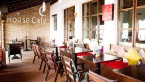 Un acogedor interior de cafetería con mesas de madera, sillas acolchadas y paredes de ladrillo irradia el encanto relajado de un "Bungalow con jacuzzi privado y cena a los pies de Sierra Nevada" mientras muestra un cartel que dice House Cafe. - ForTwo - Planes para parejas