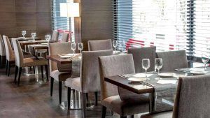 El moderno interior del restaurante, con mesas cuidadosamente dispuestas, sillas tapizadas en gris y grandes ventanales con persianas, ofrece un ambiente vibrante que recuerda a la Escapada con habitación doble, desayuno buffet y espectáculo de flamenco (Barcelona). - ForTwo - Planes para parejas
