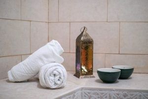 Toallas enrolladas, un farol decorativo y dos cuencos verdes crean la atmósfera tranquila de un Hammam privado en pareja en los baños árabes de Al-Haram (Granada) sobre una superficie de azulejos. - ForTwo - Planes para parejas