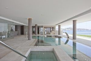 La piscina cubierta del Hotel Torre del Mar (Ibiza) presenta un diseño contemporáneo con amplios ventanales que ofrecen impresionantes vistas al mar. Los pilares de piedra realzan su elegancia, creando un remanso de paz que captura el encanto de Ibiza. - ForTwo - Planes para parejas
