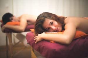 Dos personas disfrutando de un Masaje en Pareja Especial por MasVital (Granada) en MasVital en Granada, tumbados en camillas de masaje con almohadas naranjas, uno sonriendo a la cámara. - ForTwo - Planes para parejas