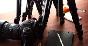 Una cámara, varios trípodes, un cuaderno y un lápiz descansan sobre una superficie de madera, capturando la esencia de una íntima "Sesión de fotografía de pareja de estudio (Madrid). - ForTwo - Planes para parejas