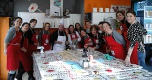 En una cocina de Madrid, un grupo alegre con delantales rojos participa en el Curso de preparación de hamburguesas premium. - ForTwo - Planes para parejas