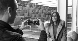Una sesión de fotografía romántica al aire libre (Barcelona) captura a una mujer sonriente con abrigo, enmarcada por macetas. Esta imagen en blanco y negro irradia el encanto de las calles de Barcelona. - ForTwo - Planes para parejas
