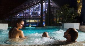 Una pareja disfruta de una noche tranquila en un jacuzzi con el resplandeciente Caldea Spa + Comida o cena para dos (Andorra) como sereno telón de fondo. - ForTwo - Planes para parejas