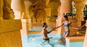 Una pareja disfruta de una cálida piscina cubierta en Caldea Spa + Comida o cena para dos (Andorra), donde la decoración de temática antigua, las estatuas y los pilares crean un ambiente encantador. - ForTwo - Planes para parejas