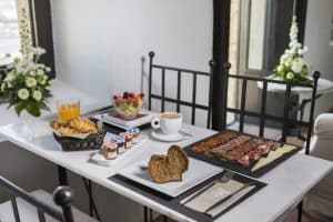 El desayuno del Hotel Torre del Canónigo (Ibiza) ofrece un delicioso menú con pan, croissants, embutidos, macedonia, café y zumo. Las vibrantes flores que lo rodean realzan el acogedor ambiente. - ForTwo - Planes para parejas