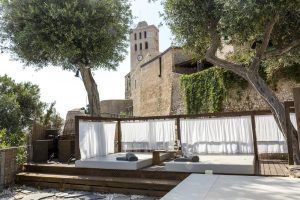 El Hotel Torre del Canónigo en Ibiza ofrece camas al aire libre con cortinas blancas bajo los árboles, cerca de la histórica torre del reloj. - ForTwo - Planes para parejas