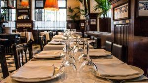 El ambiente acogedor del Restaurante 7 Portes de Barcelona queda plasmado en esta mesa elegantemente dispuesta, adornada con servilletas dobladas, vasos y un suelo a cuadros bajo una iluminación cálida. - ForTwo - Planes para parejas
