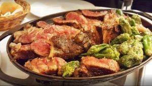 Una sartén de carnes a la parrilla con pimientos de Padrón, evocando una comida en el Restaurante 7 Portes (Barcelona), se sirve con pan de fondo. - ForTwo - Planes para parejas