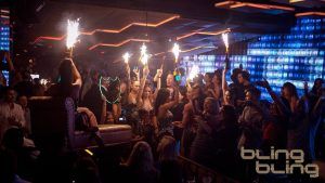 En una vibrante discoteca de Barcelona, la gente baila entre luces azules y bengalas, su emoción alimentada por la innegable atmósfera Bling Bling Barcelona. - ForTwo - Planes para parejas