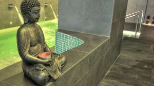 En el Hotel Sinagoga, la piscina cubierta de azulejos se ve realzada por una estatua de Buda con una vela, lo que se suma a la serenidad y al ambiente relajante de la experiencia de spa incluida en su Escapada en el Hotel Sinagoga con desayuno, bombones y spa. - ForTwo - Planes para parejas