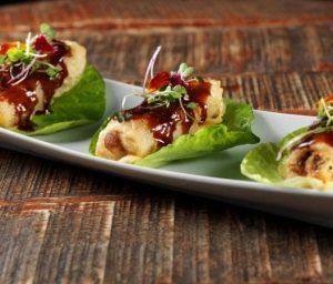 En el Restaurante Mastropiero Gastrobar de Cáceres, tres rollitos de primavera se sirven elegantemente sobre lechuga crujiente con salsa sabrosa y guarniciones, bellamente dispuestos en un plato rectangular encima de una mesa de madera rústica. - ForTwo - Planes para parejas