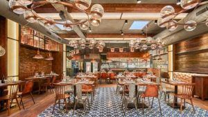 El interior rústico de la Pulpería Can Lampazas Para-lel en Barcelona cuenta con mesas de madera, sillas de metal, tuberías a la vista y lámparas colgantes esféricas que evocan el encanto de una pulpería tradicional. - ForTwo - Planes para parejas