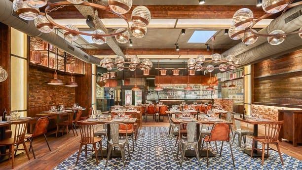 El interior rústico de la Pulpería Can Lampazas Para-lel en Barcelona cuenta con mesas de madera, sillas de metal, tuberías a la vista y lámparas colgantes esféricas que evocan el encanto de una pulpería tradicional. - ForTwo - Planes para parejas