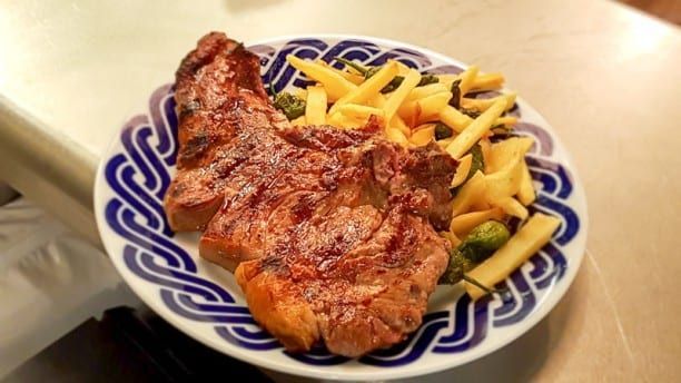 Un suculento filete, unas patatas fritas crujientes y verduras frescas se presentan elegantemente en un plato con estampado blanco y azul, evocando el vibrante estilo culinario de la Pulpería Can Lampazas Para-lel en Barcelona. - ForTwo - Planes para parejas