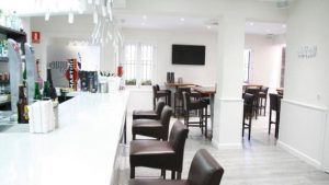 El Restaurante Bouquet en Cáceres cuenta con una moderna barra con taburetes marrones, una barra blanca, mesas altas y un televisor de pared. Su diseño luminoso y minimalista crea el ambiente ideal para una cena informal con aires de restaurante chic. - ForTwo - Planes para parejas